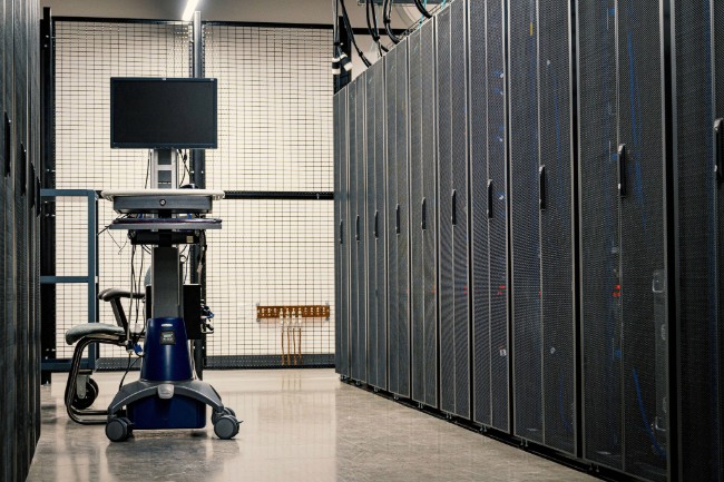Technicien SoVarNet effectuant le dépoussiérage technique et antistatique d'une baie serveur dans une salle informatique du Var